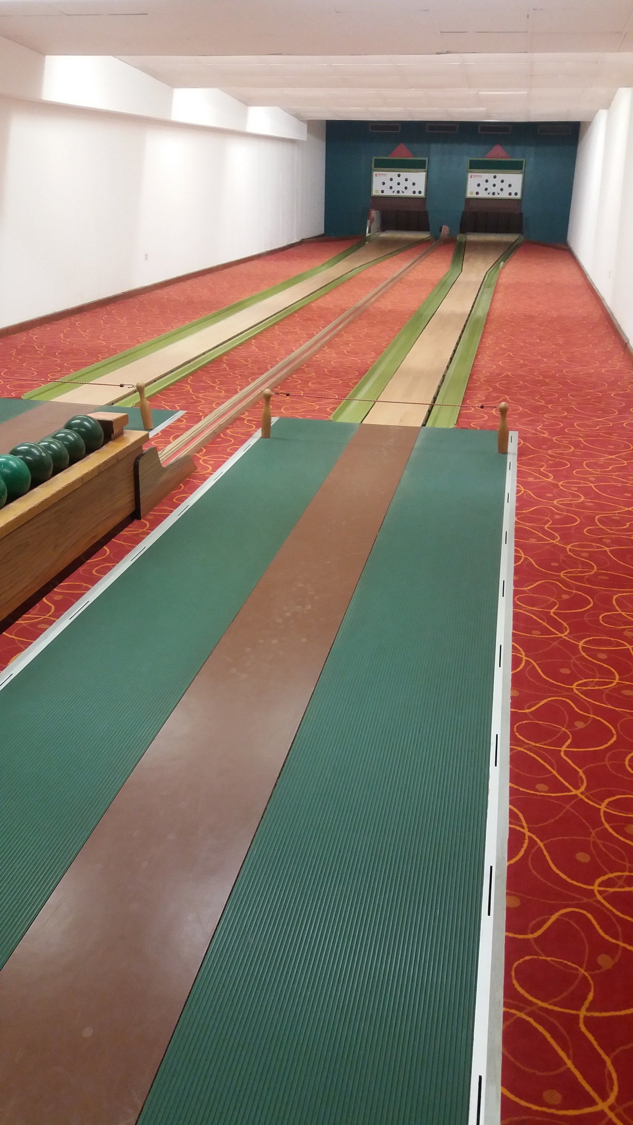 A bowling alley with green and brown lanes, a wooden bowling ball rack, and a red carpeted floor.