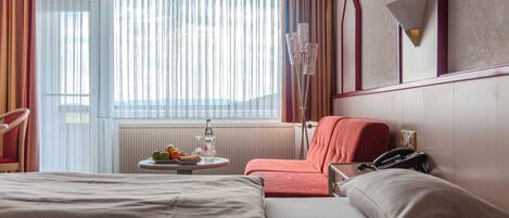 A hotel room with a bed, a chair, a table with fruit and a bottle, and a telephone.