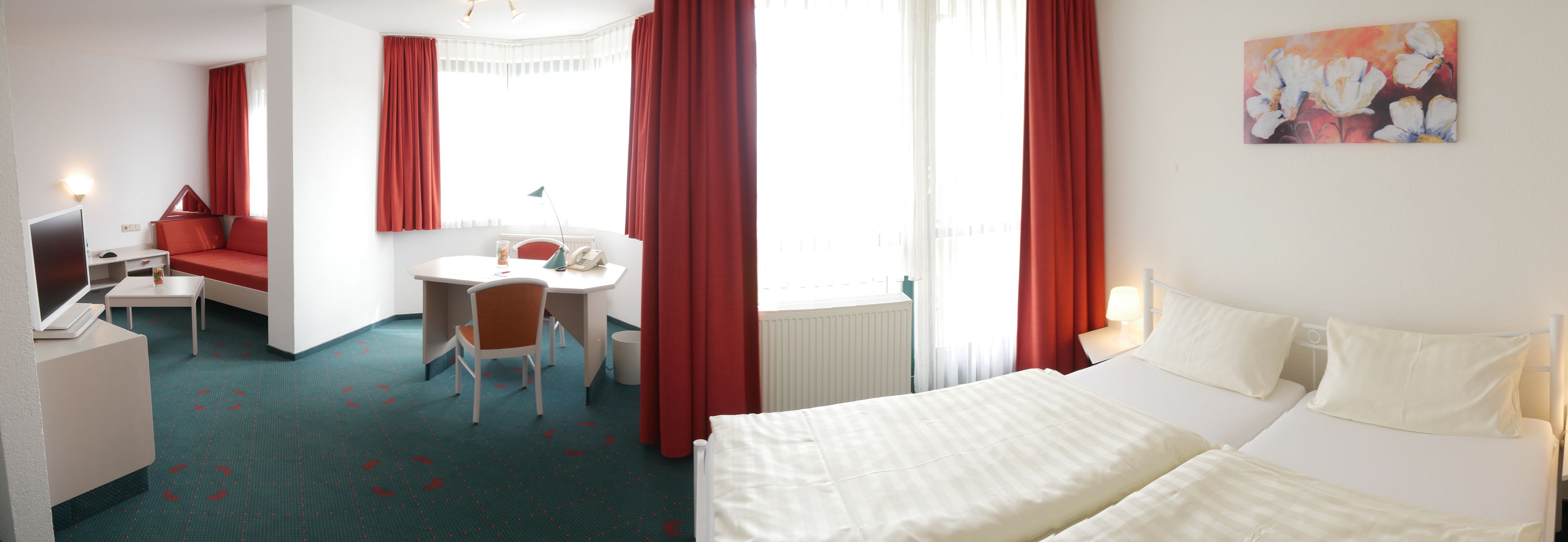 Une chambre d’hôtel avec un lit, un bureau, une chaise, une petite table et une fenêtre avec des rideaux rouges.
