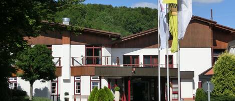 A two-story building with a balcony, a flagpole with flags, and a well-maintained garden.