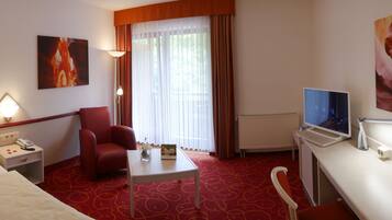 Une chambre d’hôtel avec un lit, un bureau avec un ordinateur, une chaise, une petite table avec un vase de fleurs, un téléphone et un tableau au mur.