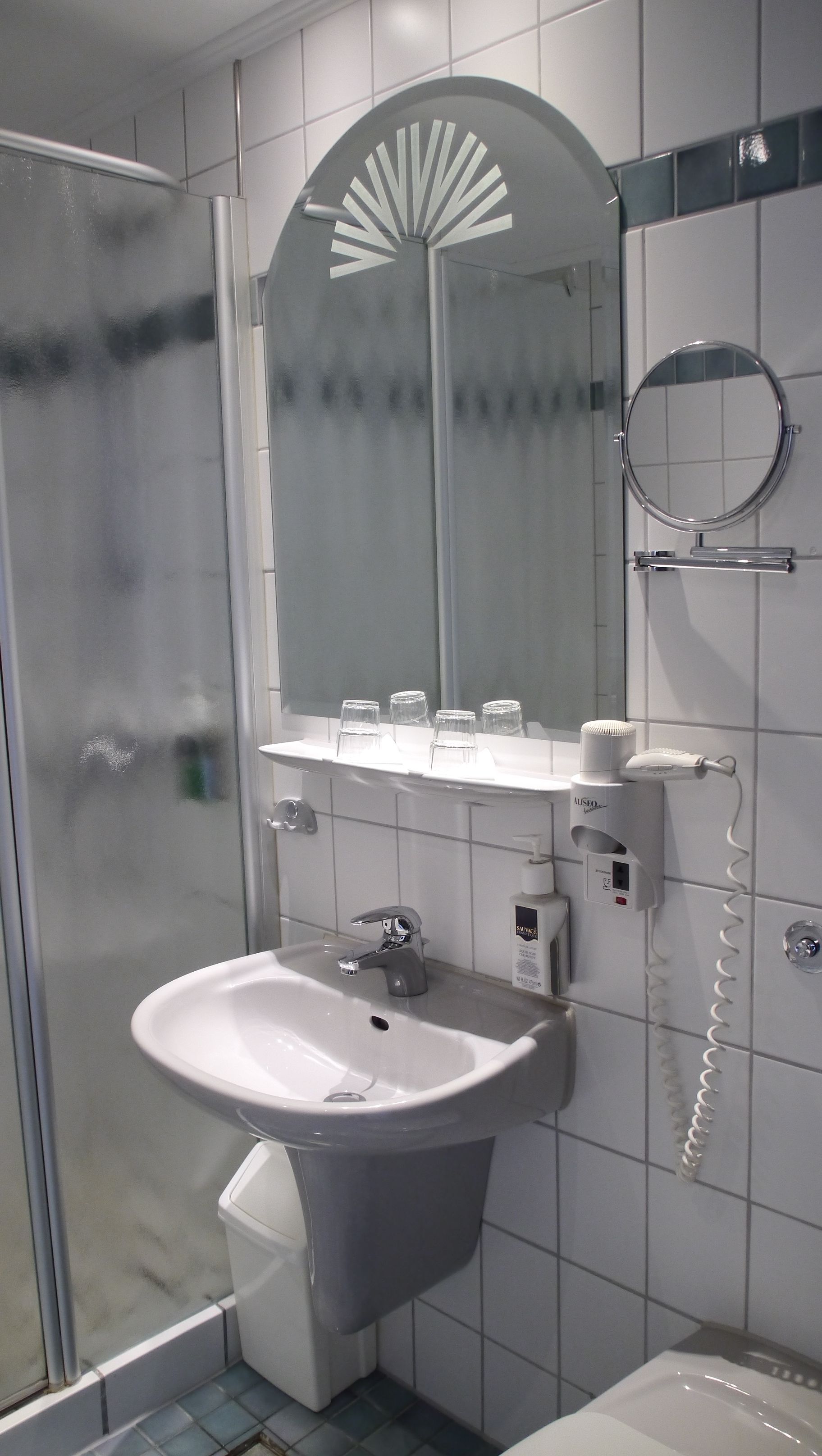 A bathroom with a glass shower enclosure, a sink with a mirror above it, and a hairdryer on the wall.
