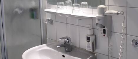 A bathroom with a glass shower enclosure, a sink with a mirror above it, and a hairdryer on the wall.