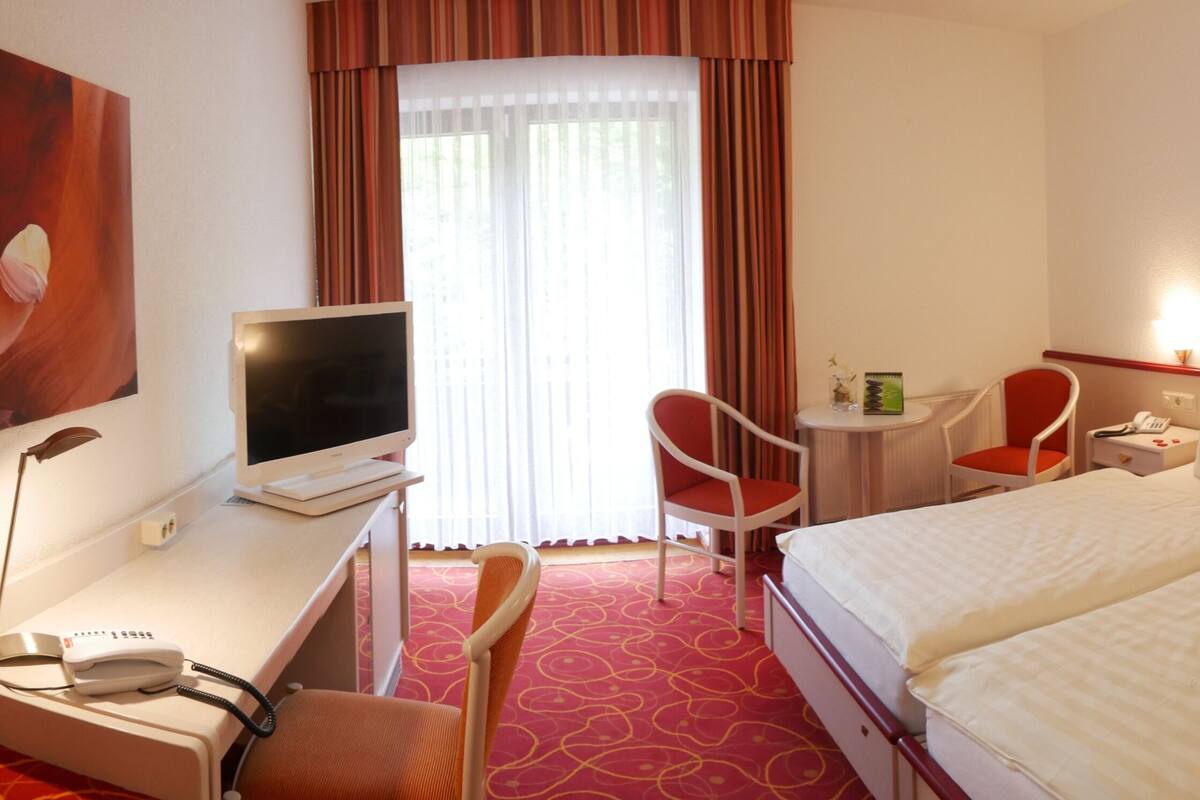 A hotel room with a bed, desk, chair, TV, and artwork on the walls.