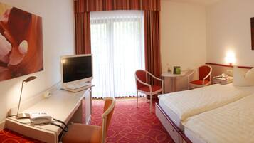 A hotel room with a bed, desk, chair, TV, and artwork on the walls.