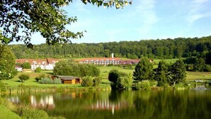 A lakeside view with a large building, possibly a hotel, surrounded by greenery and trees. - Hessen Hotelpark Hohenroda (Hohenroda)