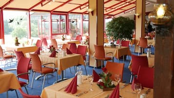 A restaurant with tables set for dining, red chairs, and a large potted plant in the center.