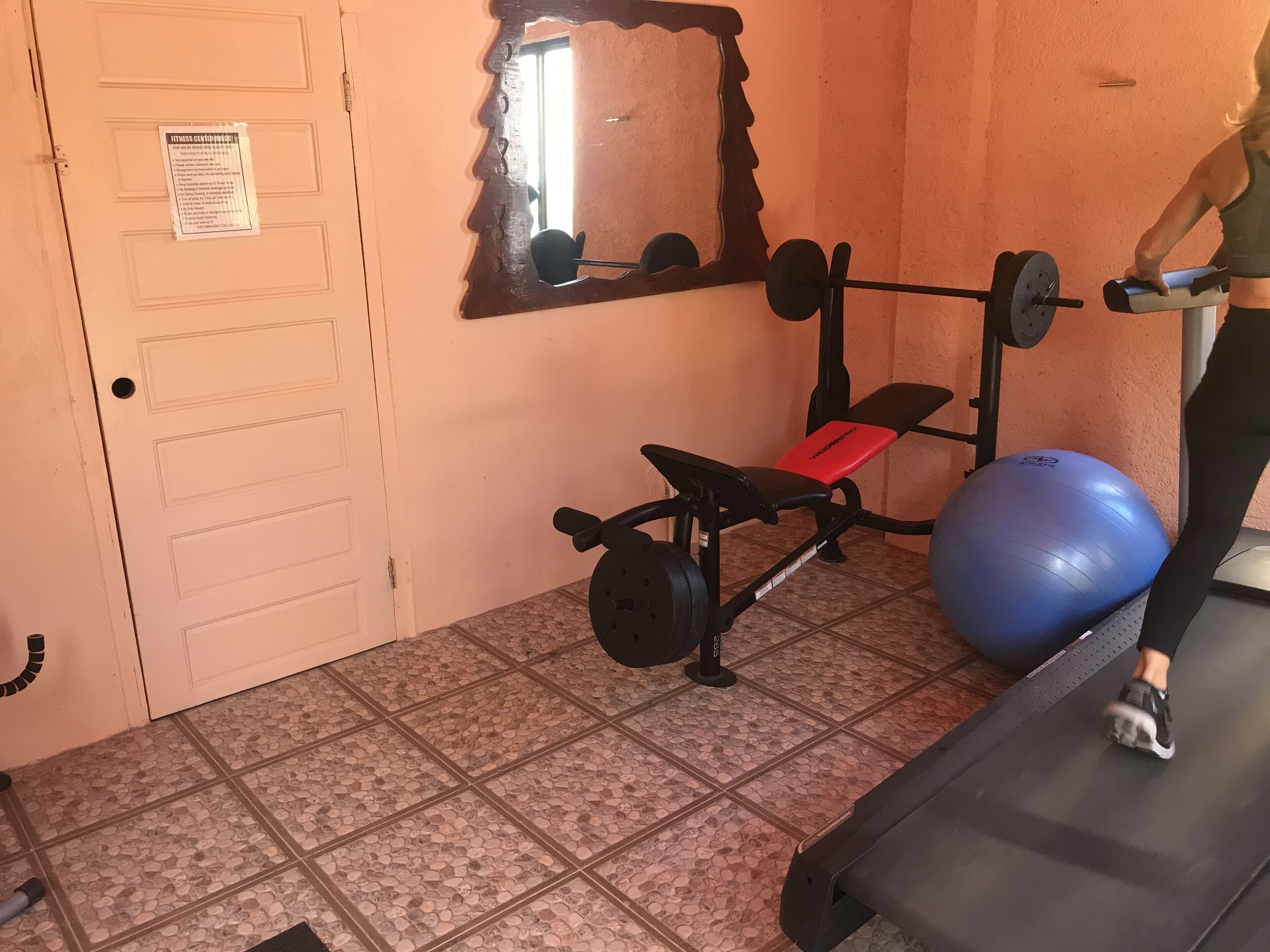 Un gimnasio con una prensa de banca, una pelota de ejercicio azul y una cinta de correr.