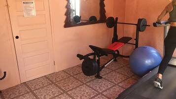 Un gimnasio con una prensa de banca, una pelota de ejercicio azul y una cinta de correr.