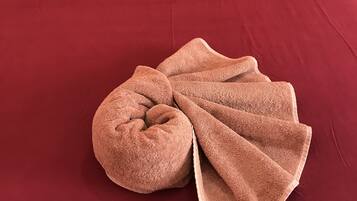 Una cama con una colcha roja, una almohada color beige y una toalla marrón doblada encima.