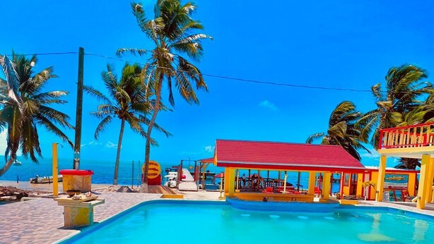 Una piscina con un edificio de techo rojo al fondo, rodeada de palmeras.