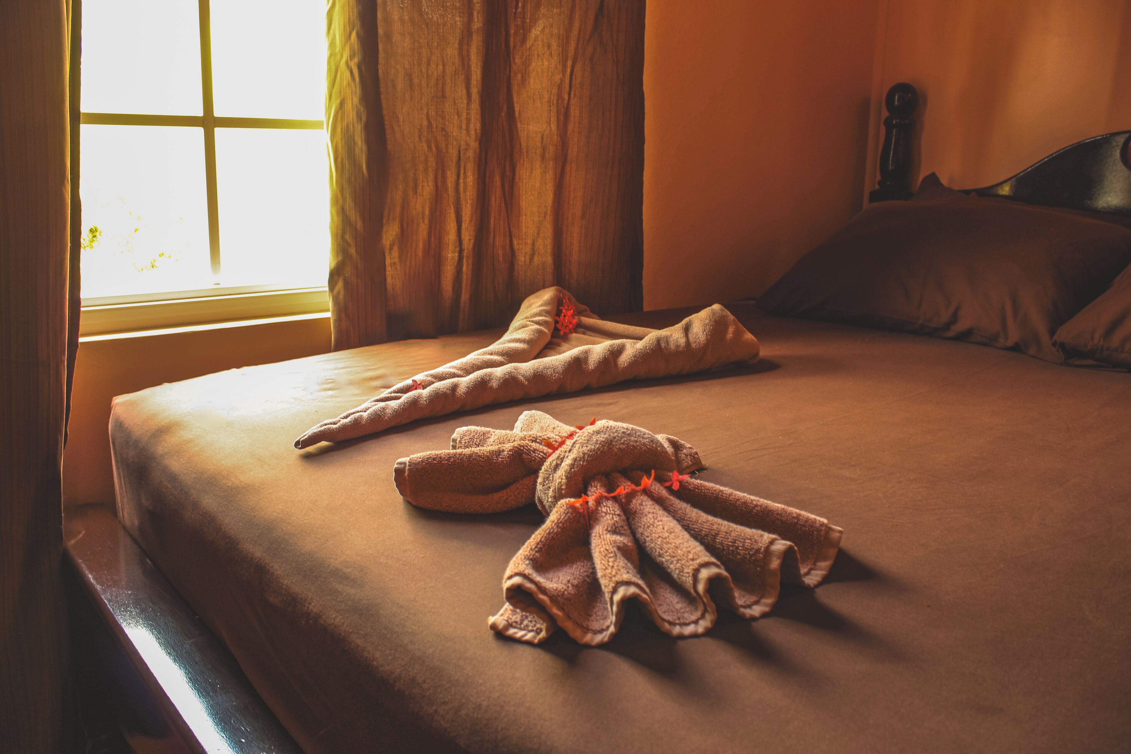 A neatly made bed with a brown bedspread and two towels arranged in a decorative manner.