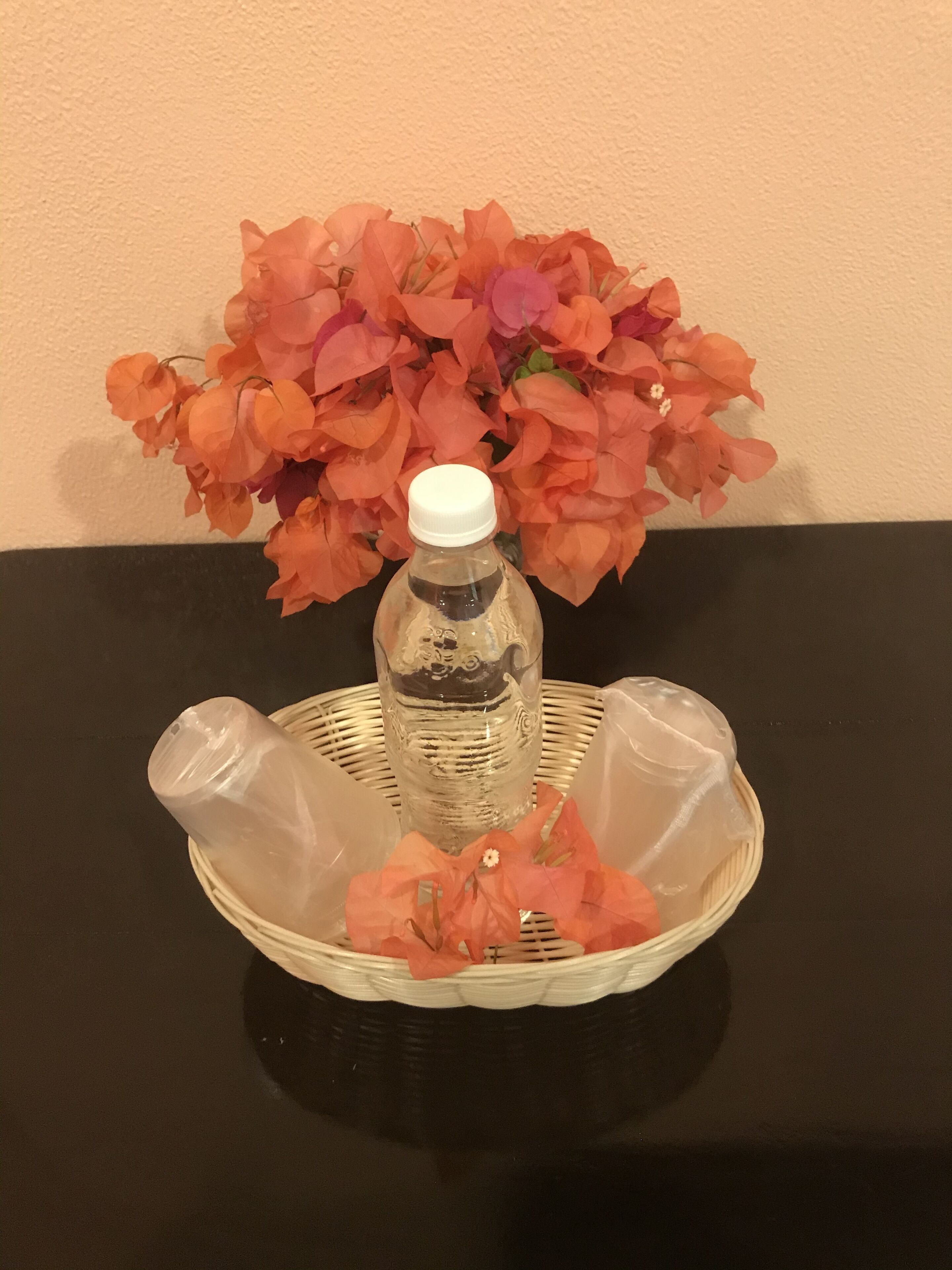 A table with a clear bottle, a basket of artificial flowers, and a plastic bag.