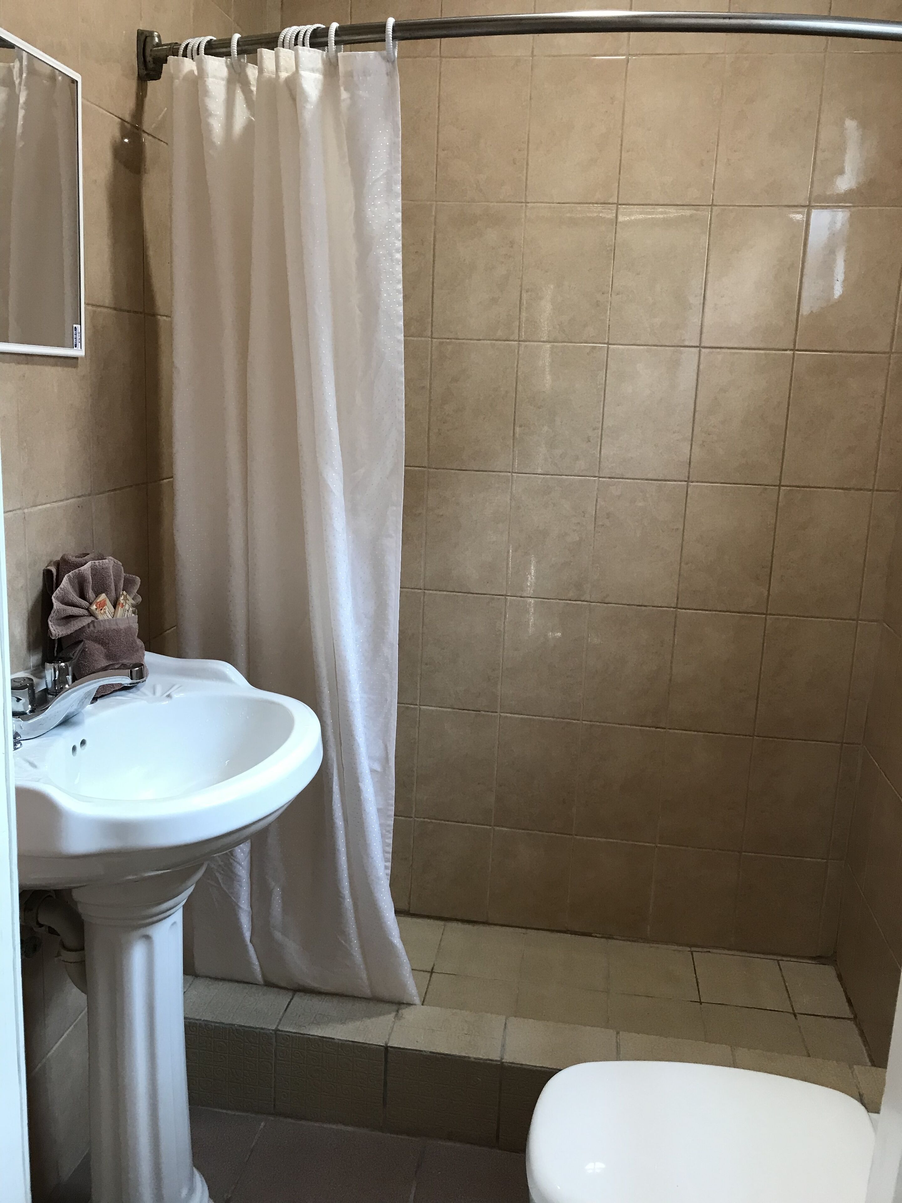 Un baño con un lavamanos blanco, un inodoro y una zona de ducha con baldosas color beige.