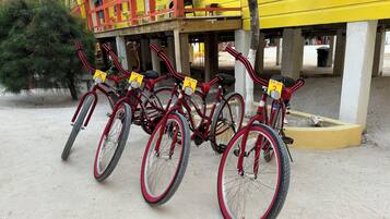 Uma fileira de bicicletas com placas numeradas, estacionadas em frente a um edifício amarelo com detalhes vermelhos.