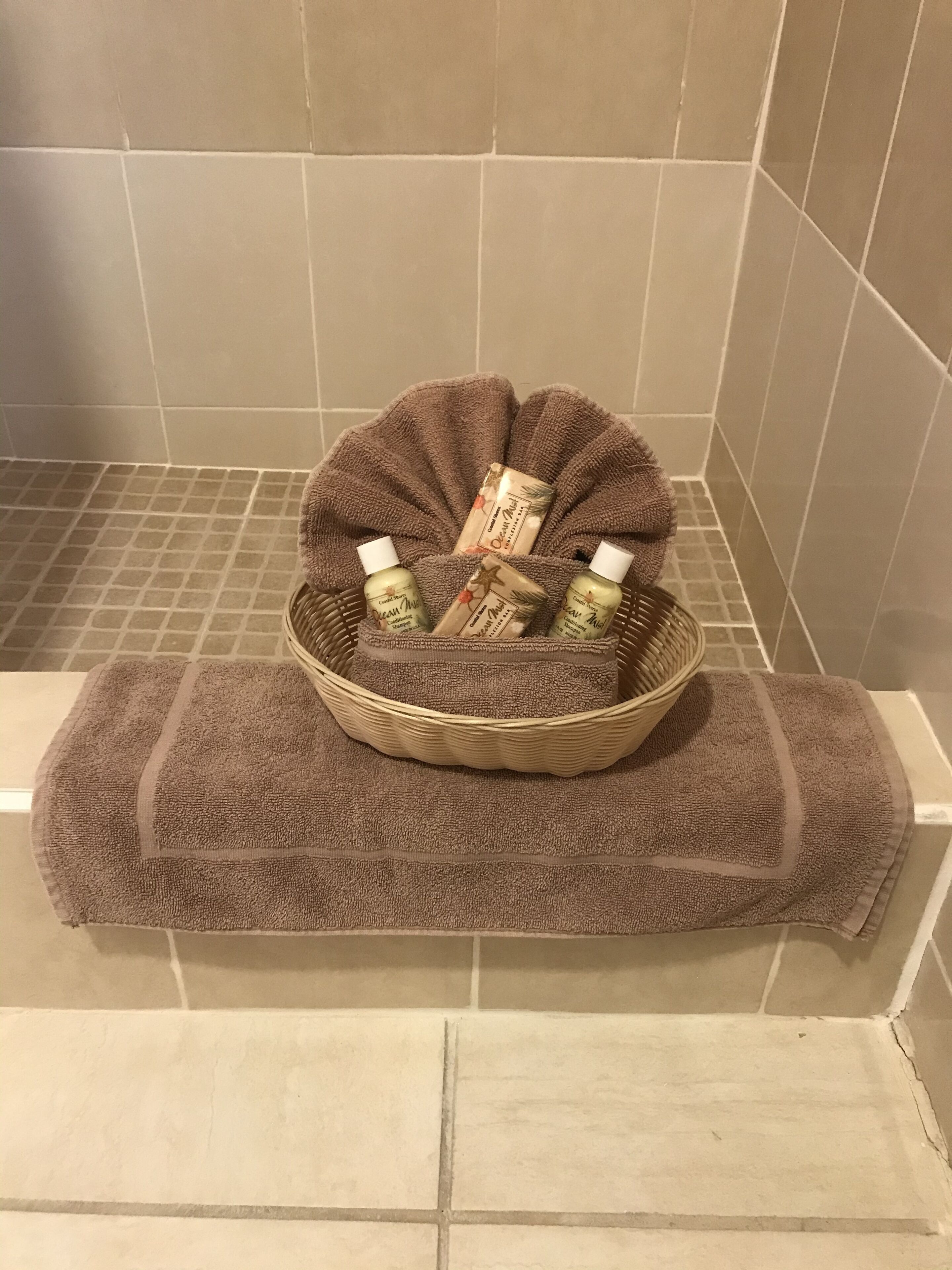 A bathroom with a bathtub, a brown towel, and a wicker basket containing bottles and a bar of soap.