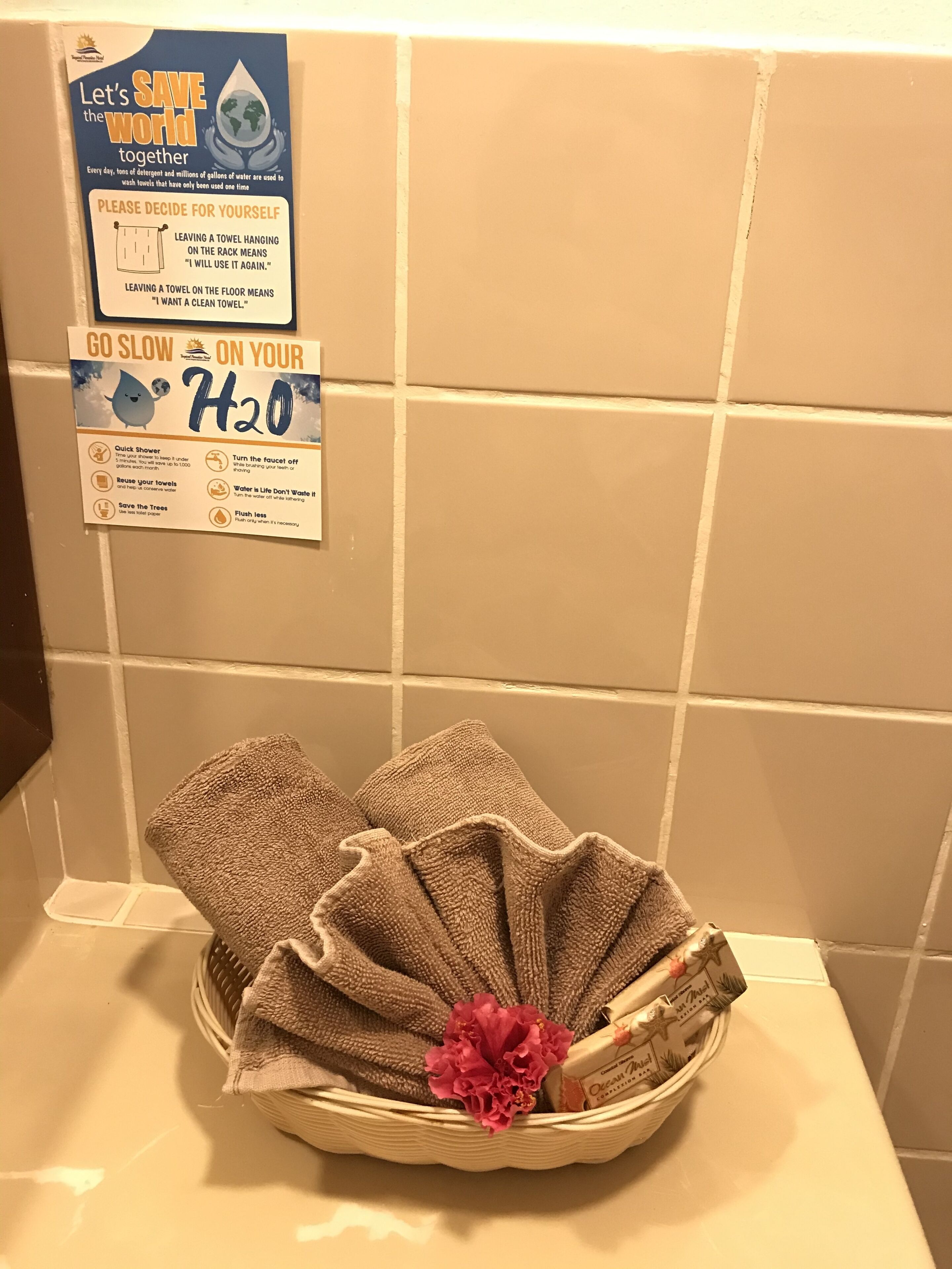 A bathroom with a sign promoting water conservation and a basket with towels and a flower.