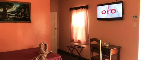 A room with two beds, a television, a painting, and a window with curtains.