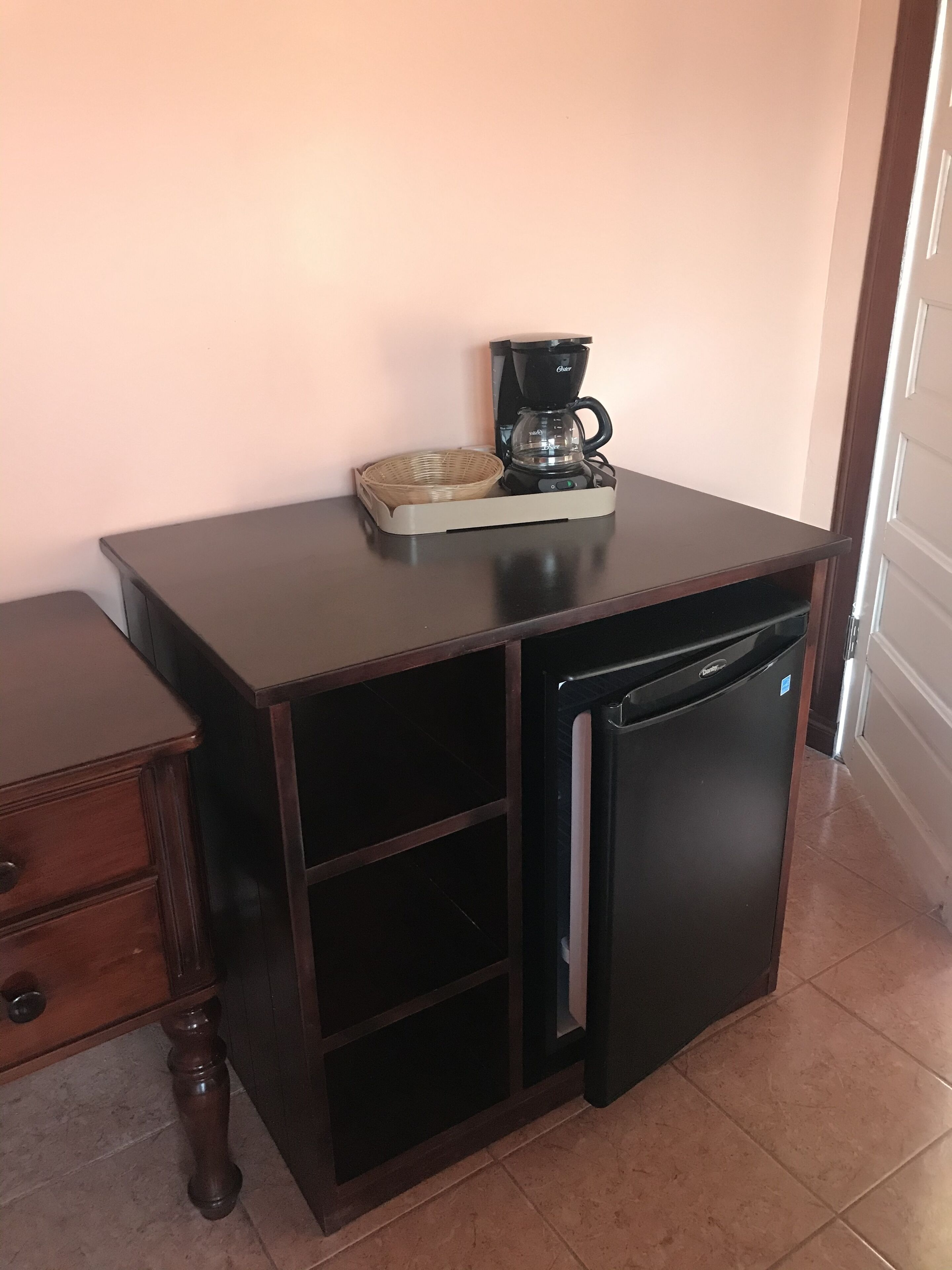 A compact kitchen area with a coffee maker, a small refrigerator, and a wooden cabinet with drawers.