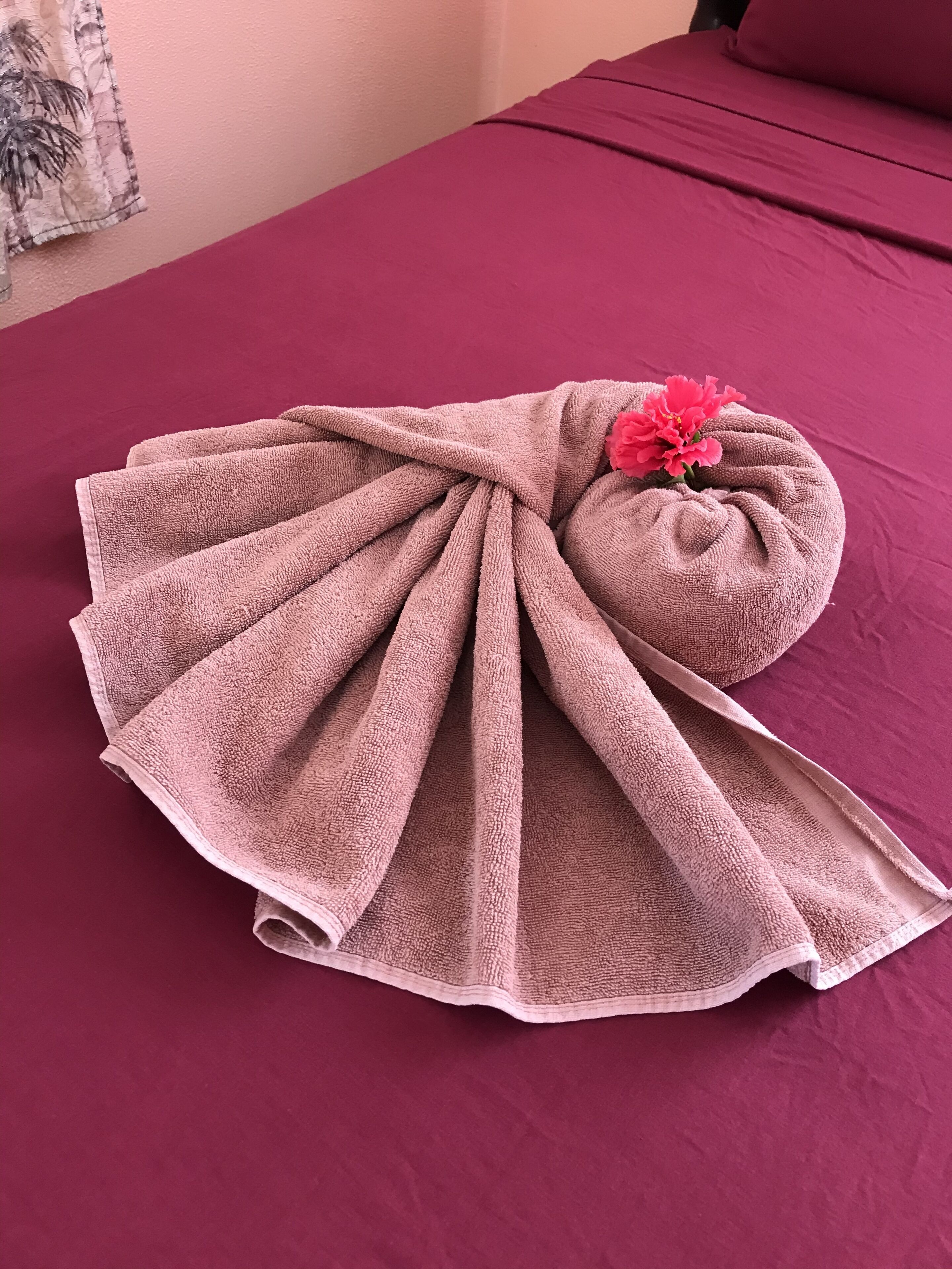 Una toalla doblada con una flor rosa sobre una cama con cubrecama rosa.