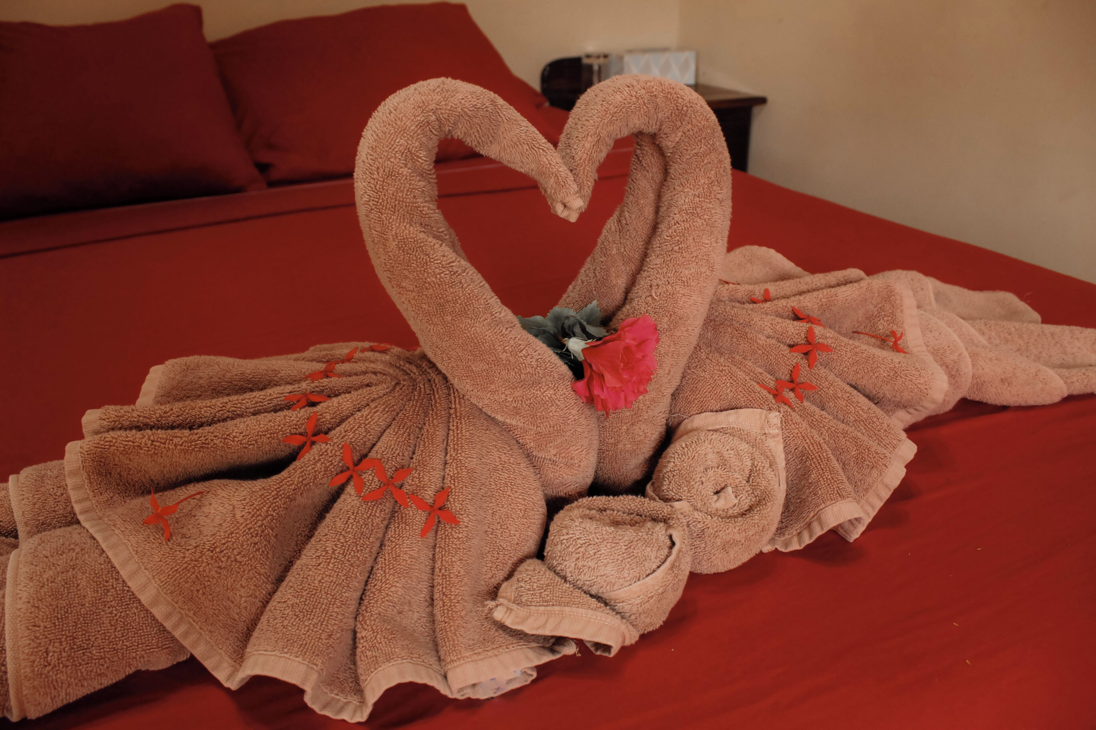 Una cama con una cubierta roja y una decoración de toallas con forma de cisne.