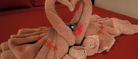 A bed with a red cover and a towel arrangement in the shape of a swan.