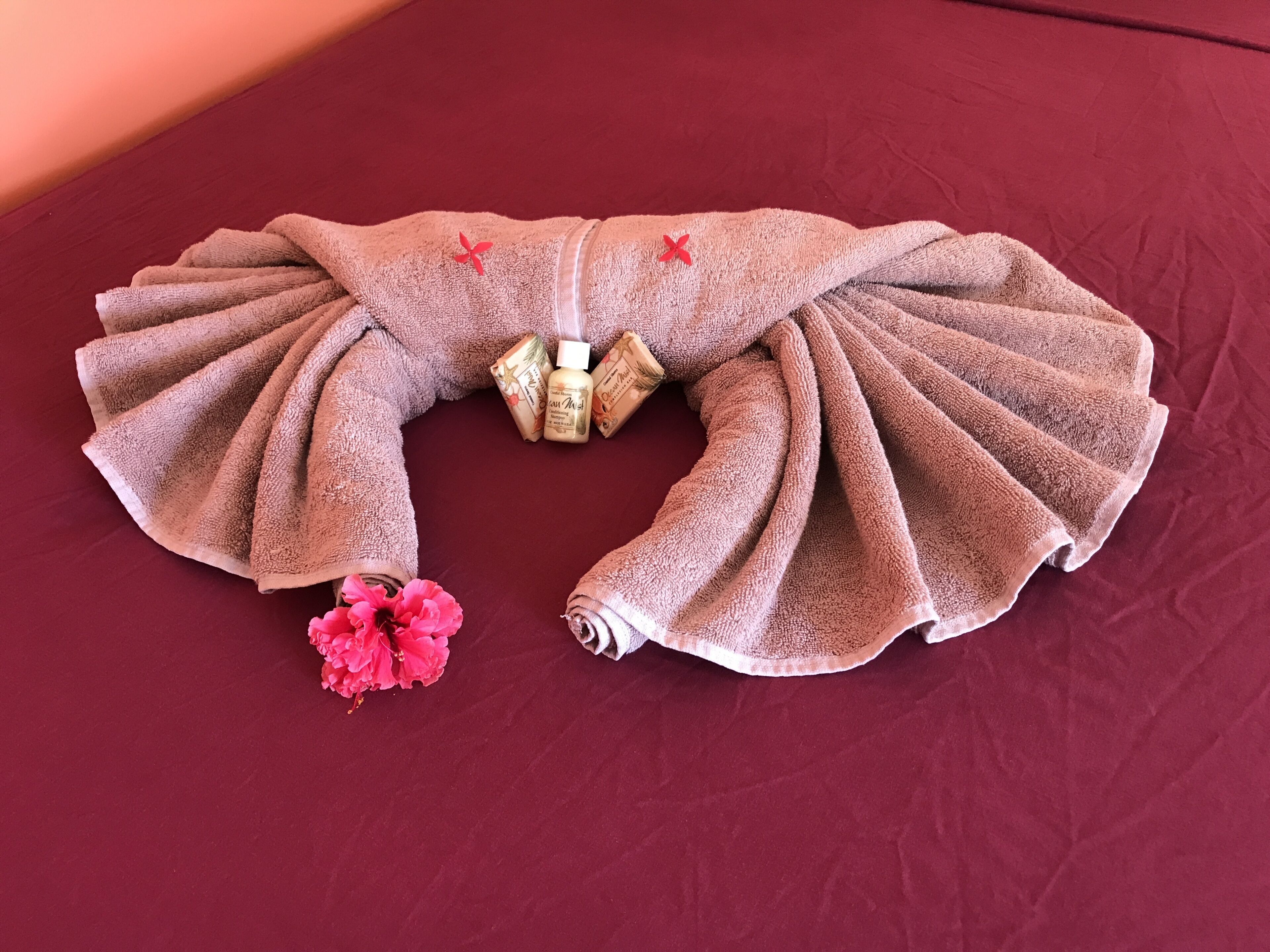 Ein Handtuch als Fächer drapiert, mit einer rosa Blume und Toilettenartikeln auf roter Oberfläche.