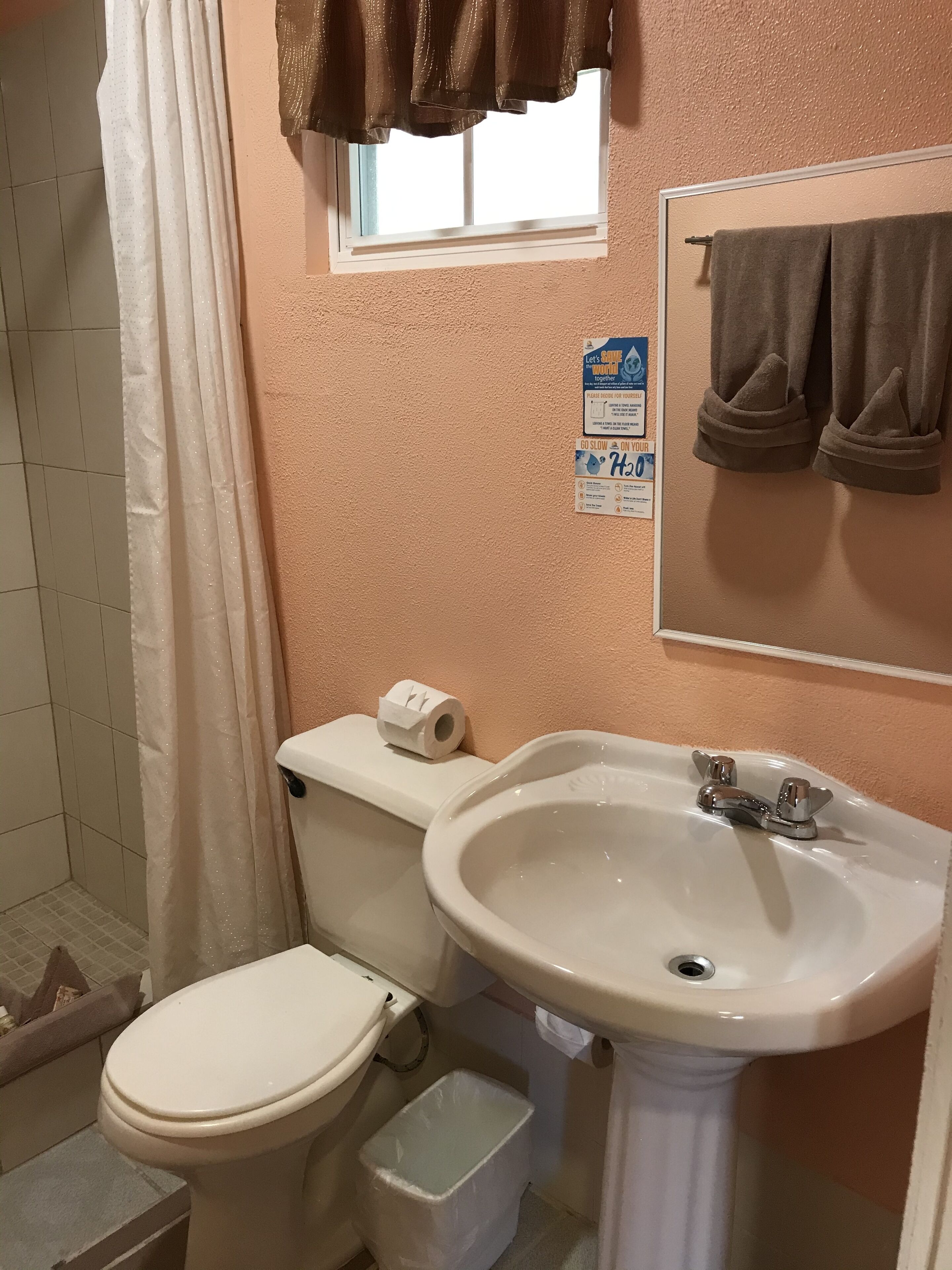A bathroom with a toilet, sink, and shower curtain. There are towels hanging on the wall and a sign above the sink.