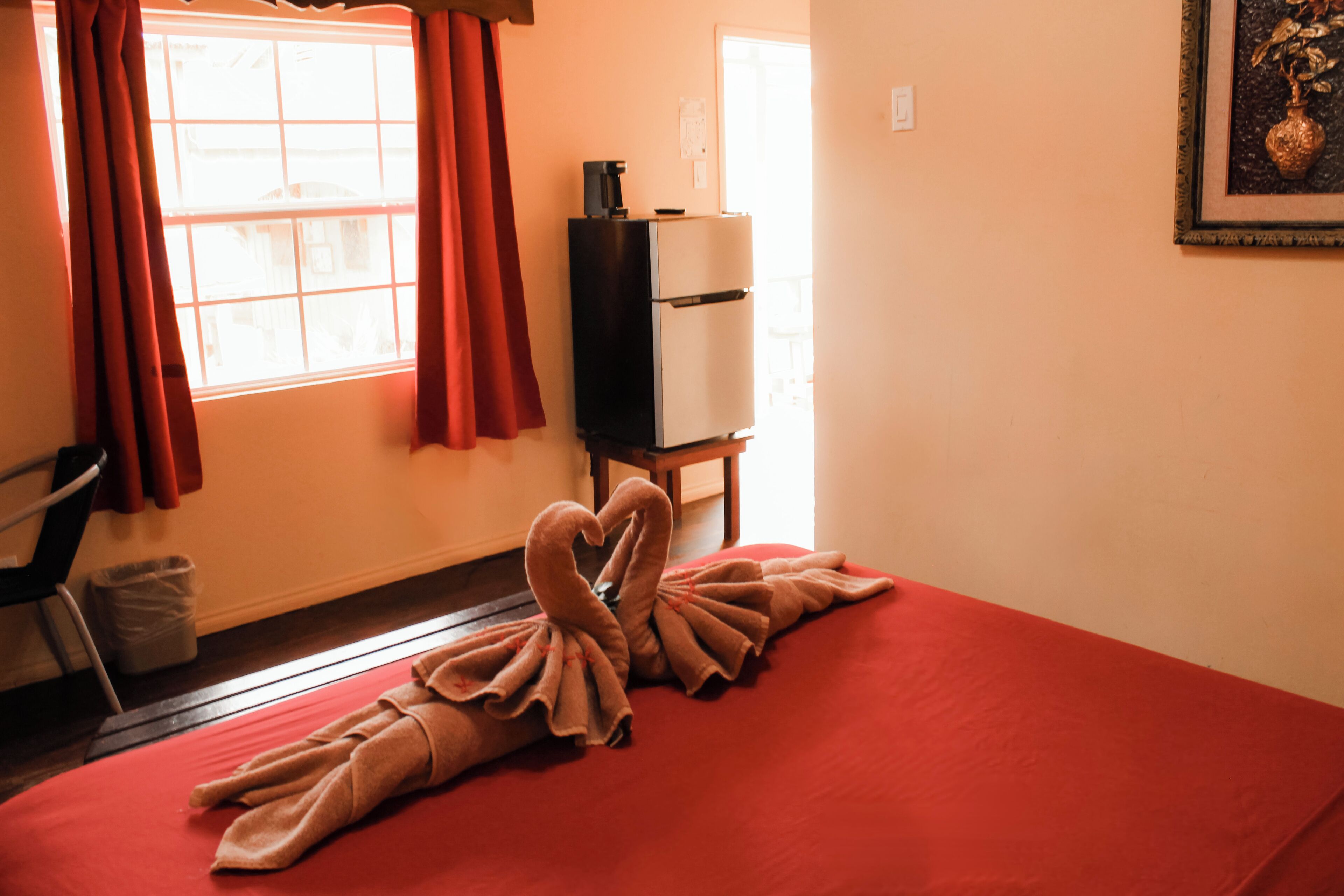 Una habitación de hotel con una colcha roja, una cafetera sobre un mueble blanco y un cuadro en la pared.