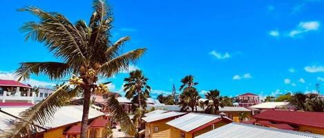 A row of wooden buildings with red roofs, a palm tree, and a clear blue sky.