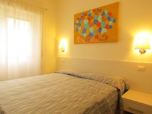 A hotel room with a bed, two bedside lamps, a nightstand, and a painting on the wall. - Buonarroti Guest House (Rome)