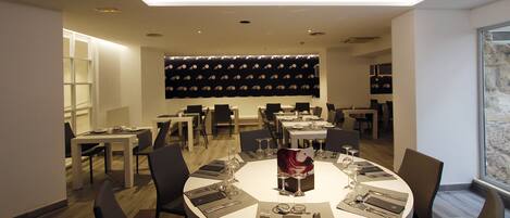 A modern dining area with round tables set for six, equipped with cutlery and wine glasses.