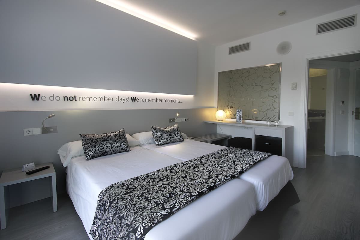 Ein modernes Hotelzimmer mit einem großen Bett, Nachttischen, einem Spiegel und einem motivierenden Zitat an der Wand.