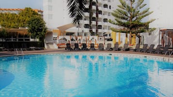 A swimming pool with lounge chairs and a building with balconies in the background.
