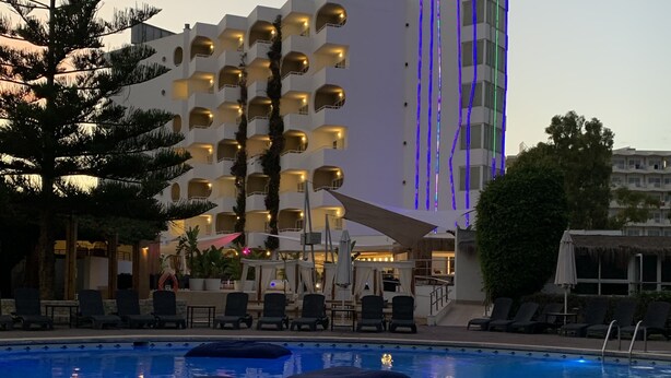 Un hotel con piscina, sillas de descanso y un edificio alto con franjas iluminadas.