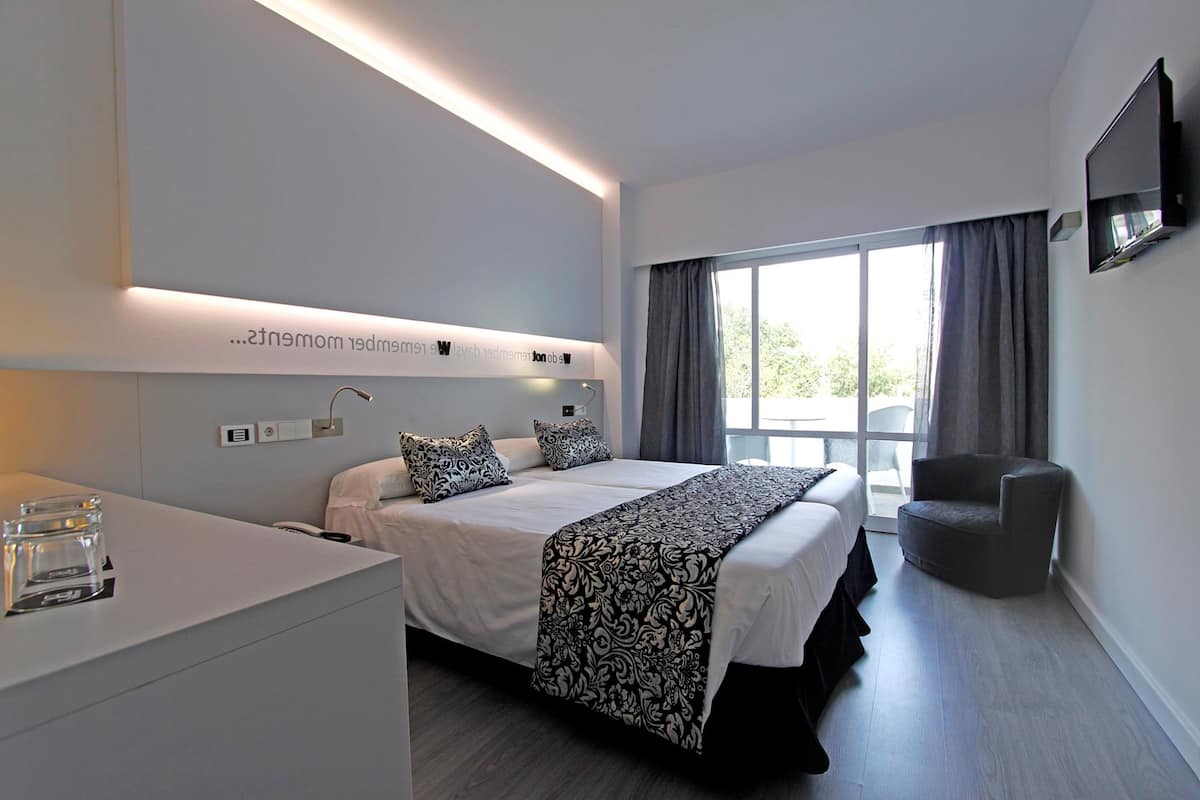 Ein modernes Hotelzimmer mit einem großen Bett, Nachttischen, einem Flachbildfernseher und Blick ins Freie.