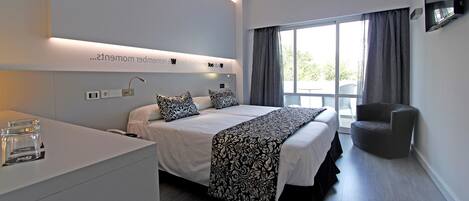 Habitación de hotel moderna con una cama grande, mesitas de noche, un televisor de pantalla plana y vistas al exterior.