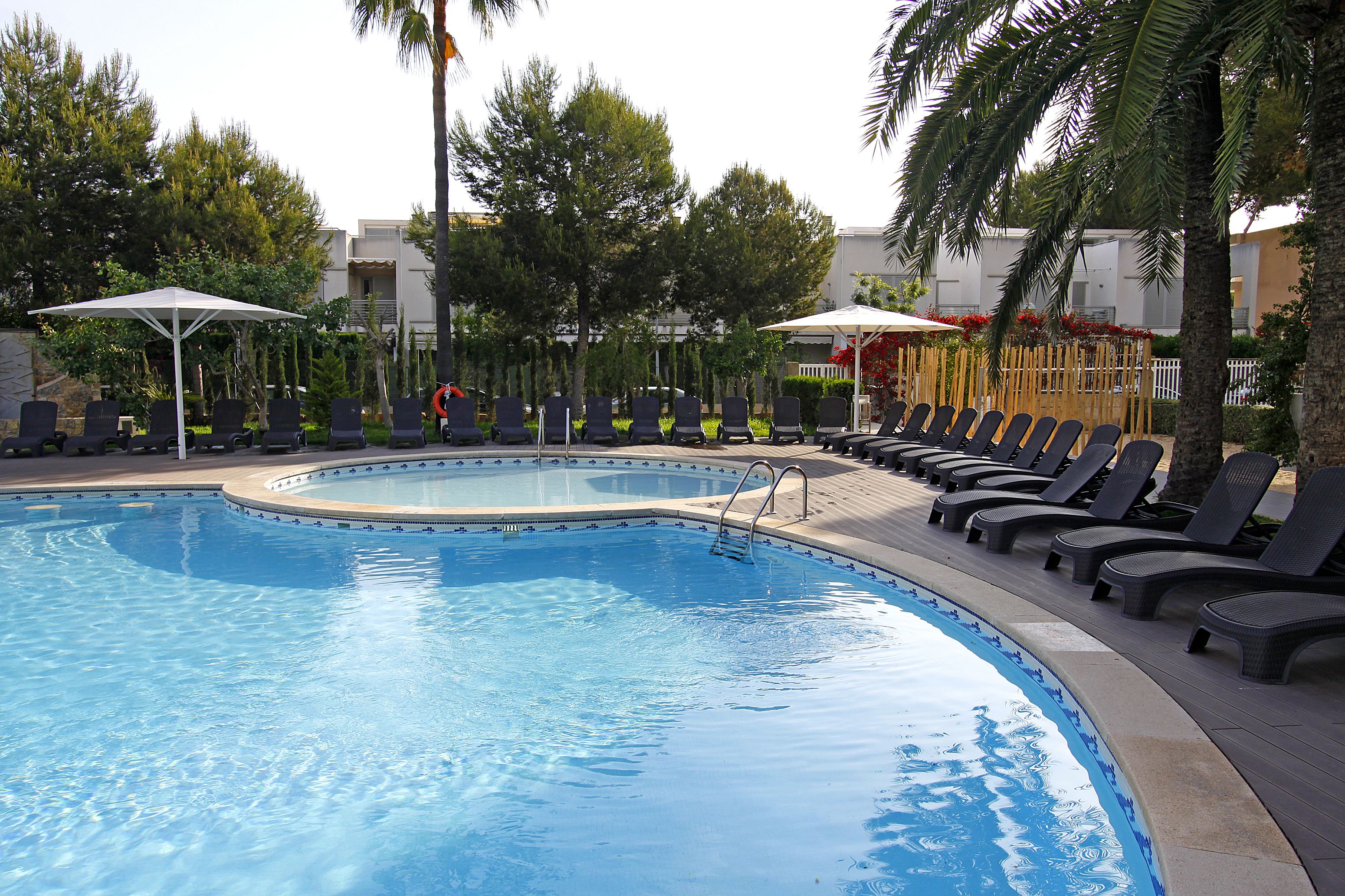 A swimming pool with lounge chairs and umbrellas, surrounded by trees and buildings.