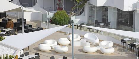 An outdoor seating area with modern chairs and tables, surrounded by white umbrellas and a glass balustrade.