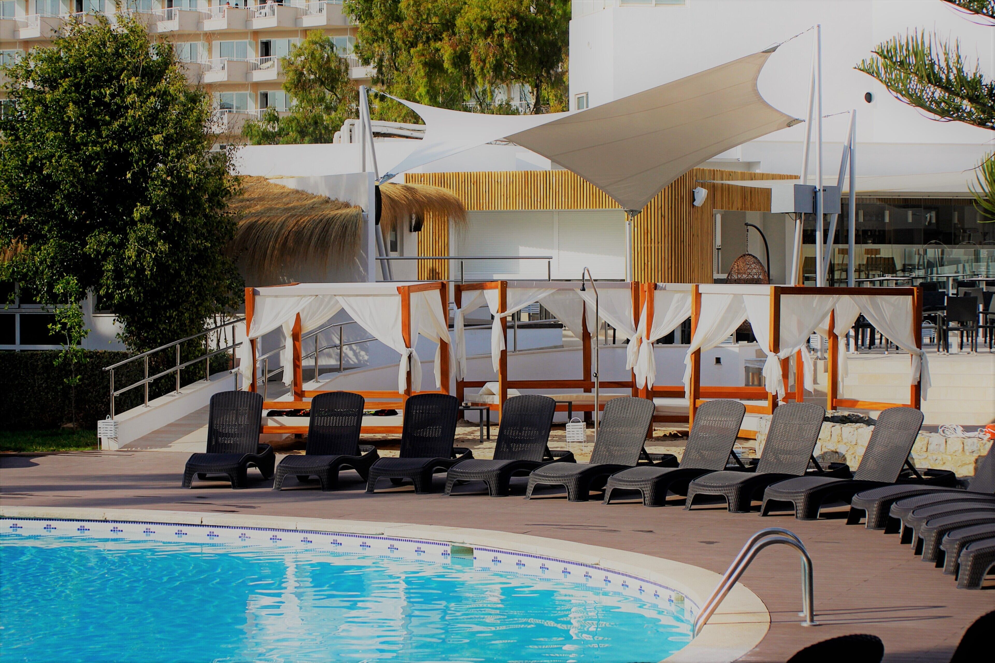 A poolside area with lounge chairs and umbrellas, a pool, and a building with a modern design.