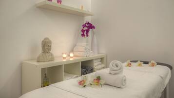 Relax in a serene spa room with a neatly made bed, candles, and a vase of flowers.