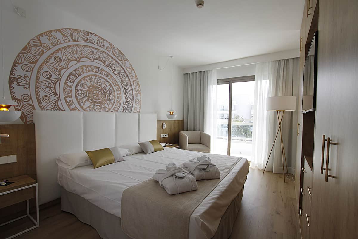 A hotel room with a large bed, a chair, a desk, a wardrobe, and a large circular wall decoration.