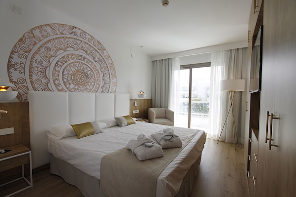A hotel room with a large bed, a chair, a desk, a wardrobe, and a large circular wall decoration. - BG Hotel Rei del Mediterrani (Muro)