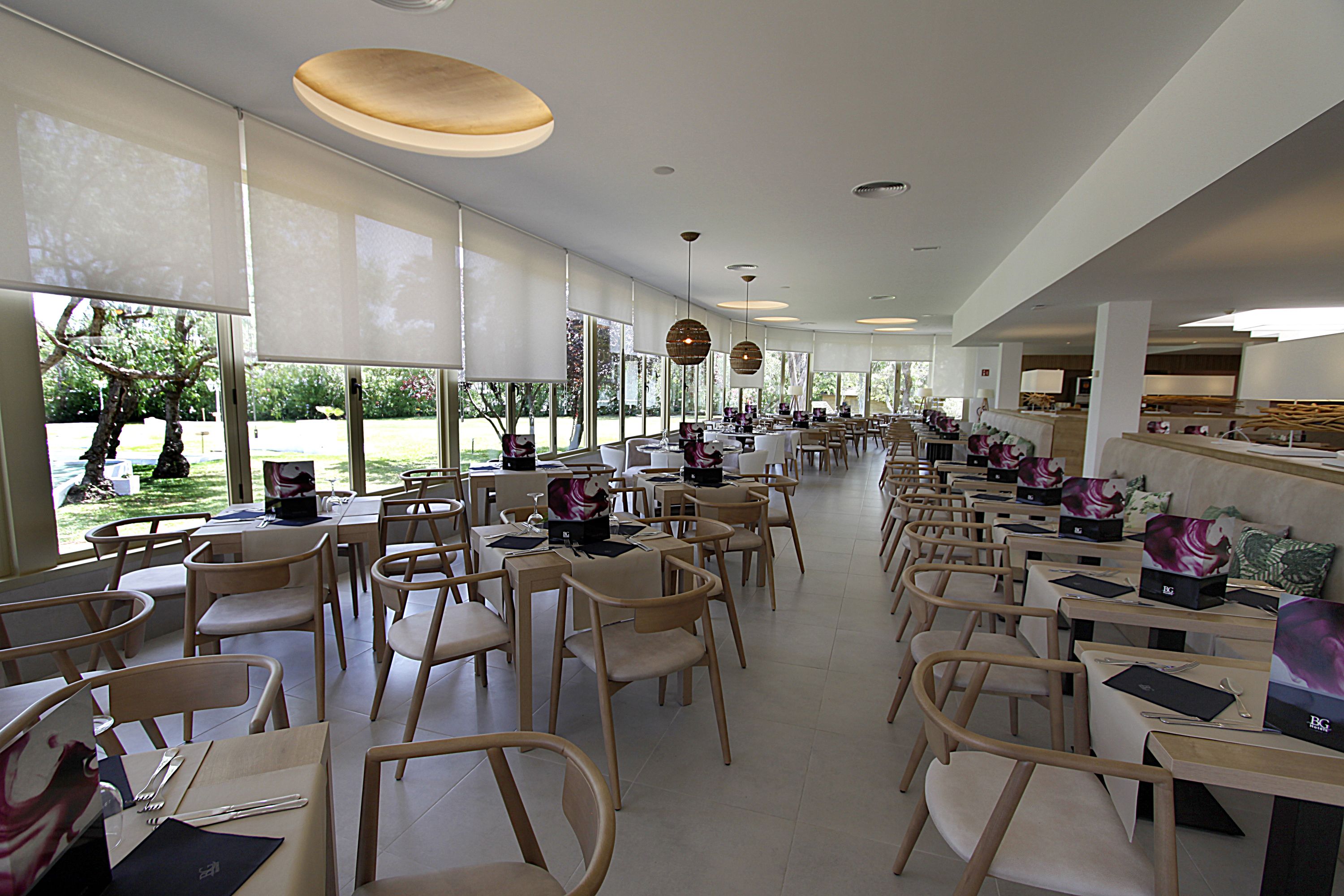 Un comedor espacioso con varias mesas y sillas, ventanas amplias e iluminación colgante.