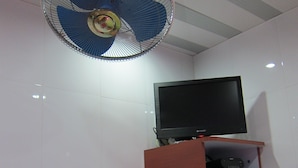 A room with a television on a wooden shelf, a fan on the ceiling, and a green bowl on a table. - Guangdong Guest House (Kowloon)