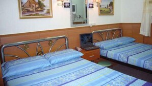 A hotel room with two single beds, each with a blue patterned bedspread and pillows. There are two wall-mounted lamps, and a framed picture of a house is above the left bed. - Guangdong Guest House (Kowloon)
