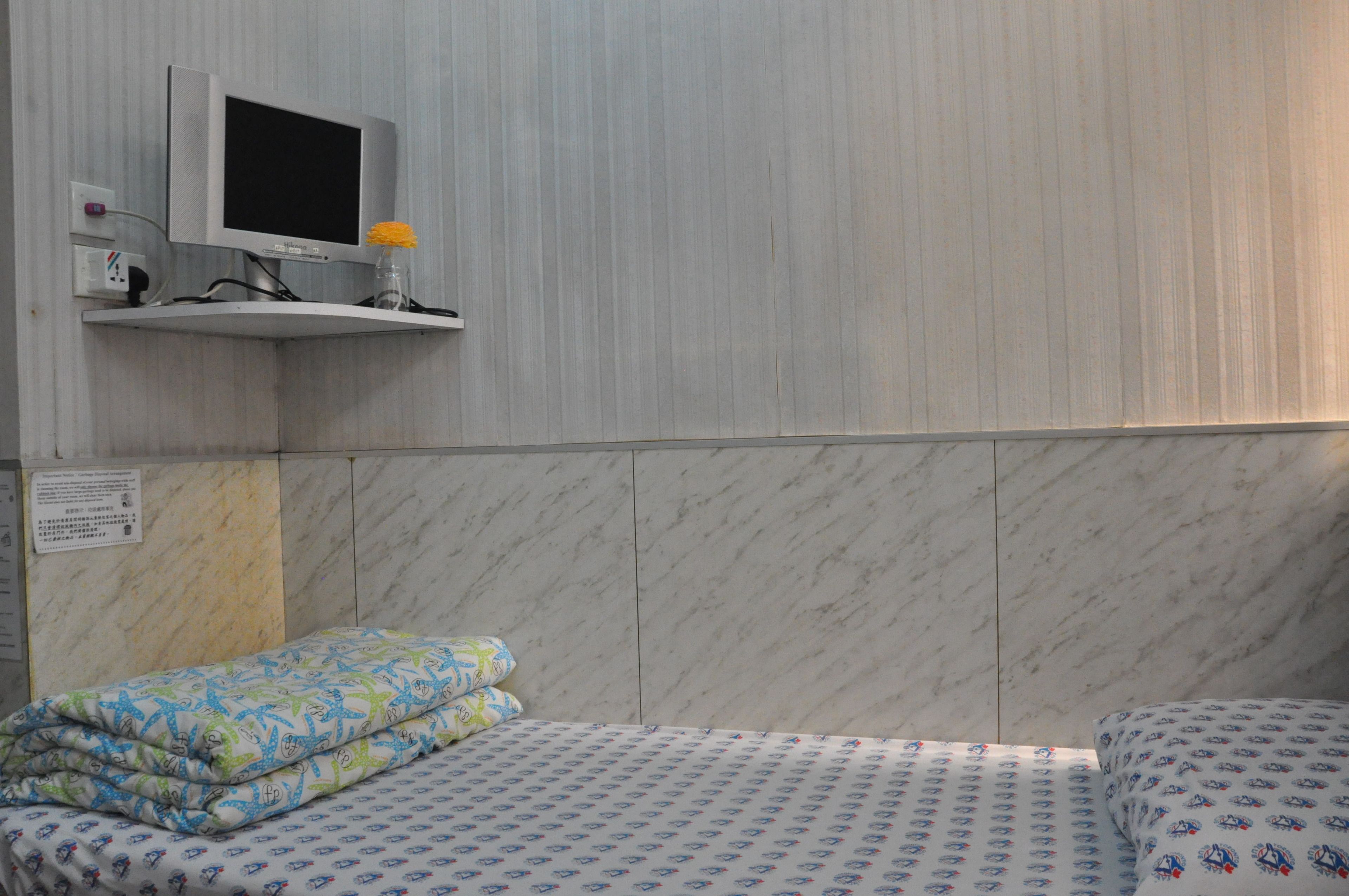 A hotel room with a bed, a TV mounted on the wall, and a small shelf with a vase.