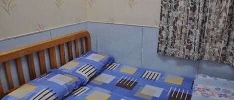 A room with a wooden bed, blue and white patterned bedding, floral curtains, and a patterned wall.