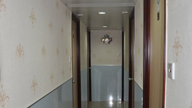 Un pasillo con papel tapiz estampado, suelo de baldosas y puertas que dan a varias habitaciones.