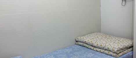 Una habitación pequeña con cama individual, colcha de flores azules y almohada con motivos florales coloridos.